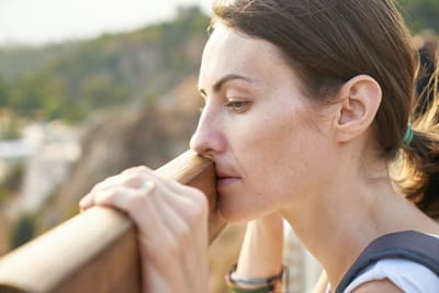 lady thinking while looking over a fence outdoors at sunset